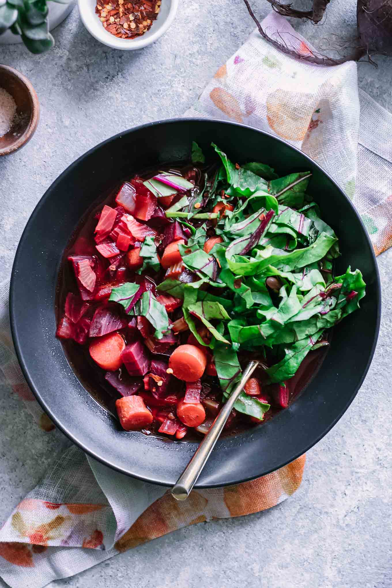 beet vegetable soup with chopped beet greens in a black bowl on a blue table