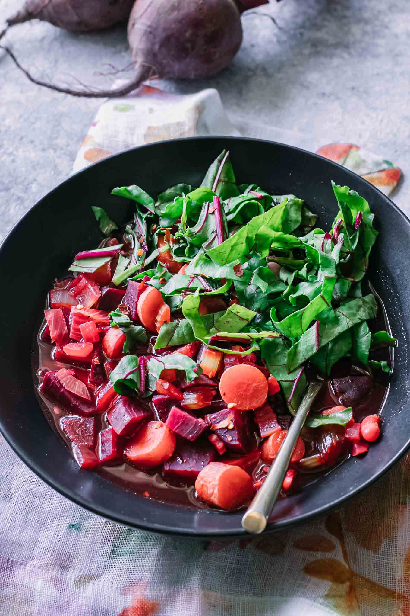 a bowl of beet vegetable soup on a blue table with beet greens