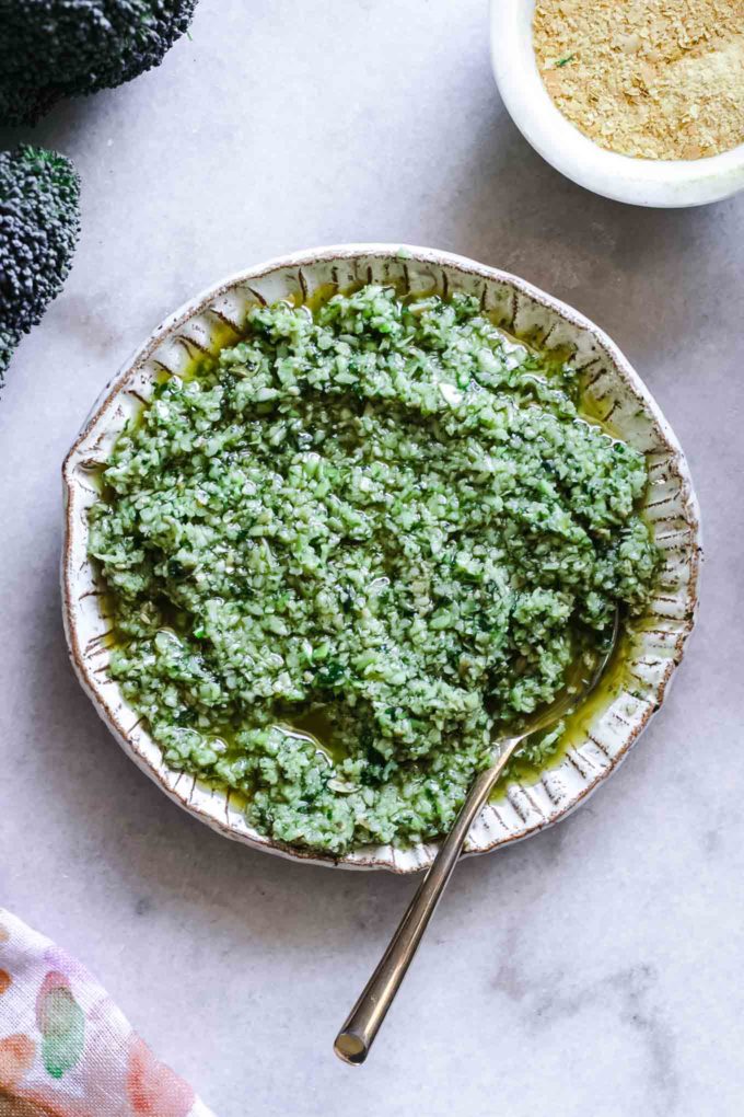 a bowl of pesto with broccoli on a white countertop