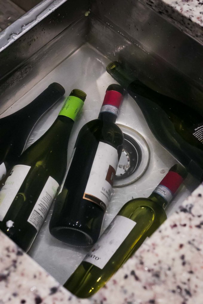 wine bottles soaking in a sink full of water, vinegar, and dish soap