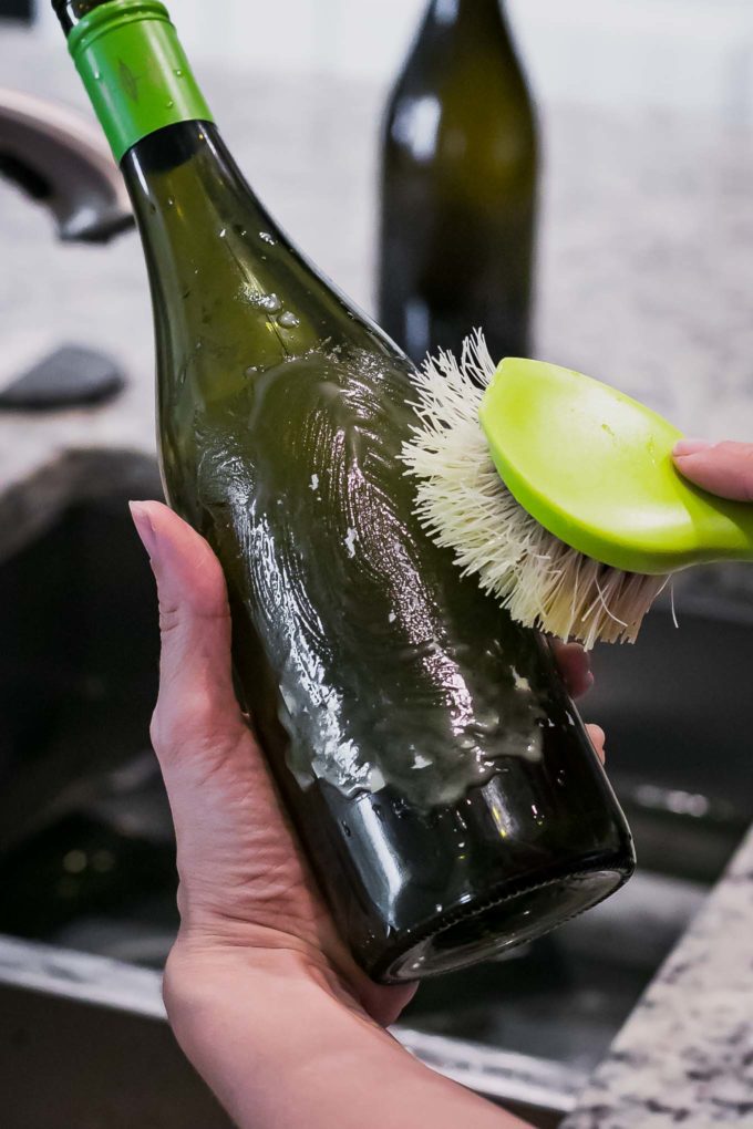 a hand scrubbing a label off a wine bottle with a wooden scrub brush