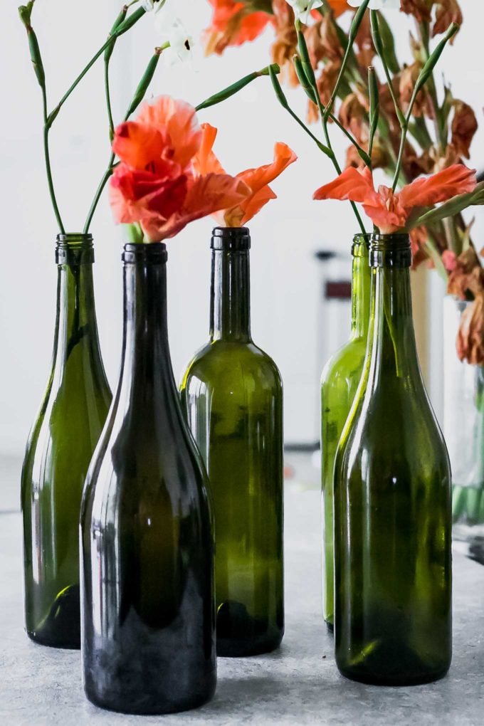 wine bottle flower vases with orange flowers on a white table