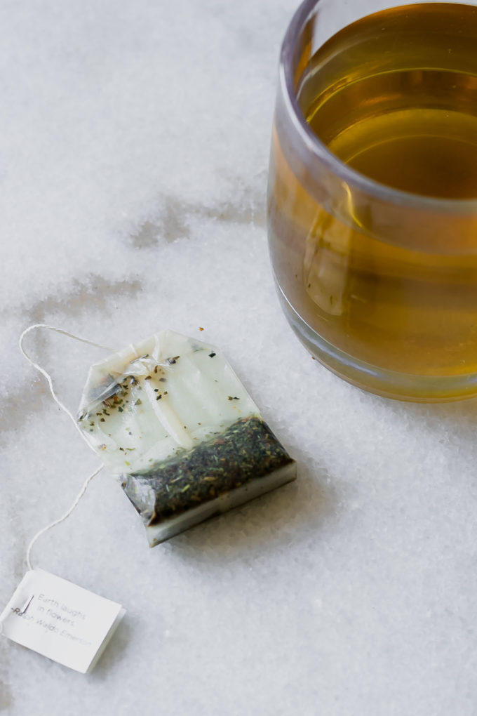 a used tea bag on a white table next to a mug of brewed tea