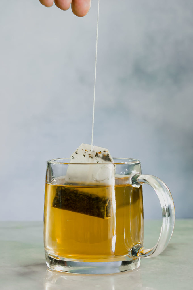 a hand pulling a tea bag out of a glass tea mug