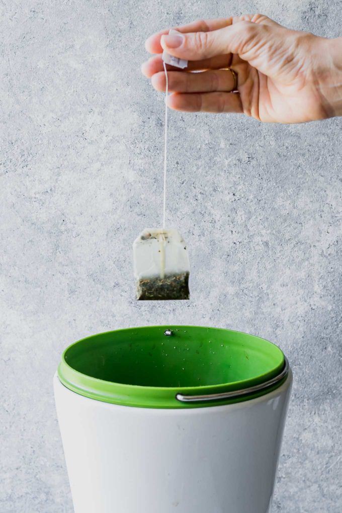 a hand dropping a used tea bag into a compost bin