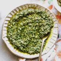 pumpkin seed pesto on a white plate on a white table with bowls of pumpkin seeds and salt
