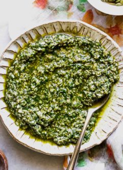 pumpkin seed pesto sauce in a white bowl with a gold fork