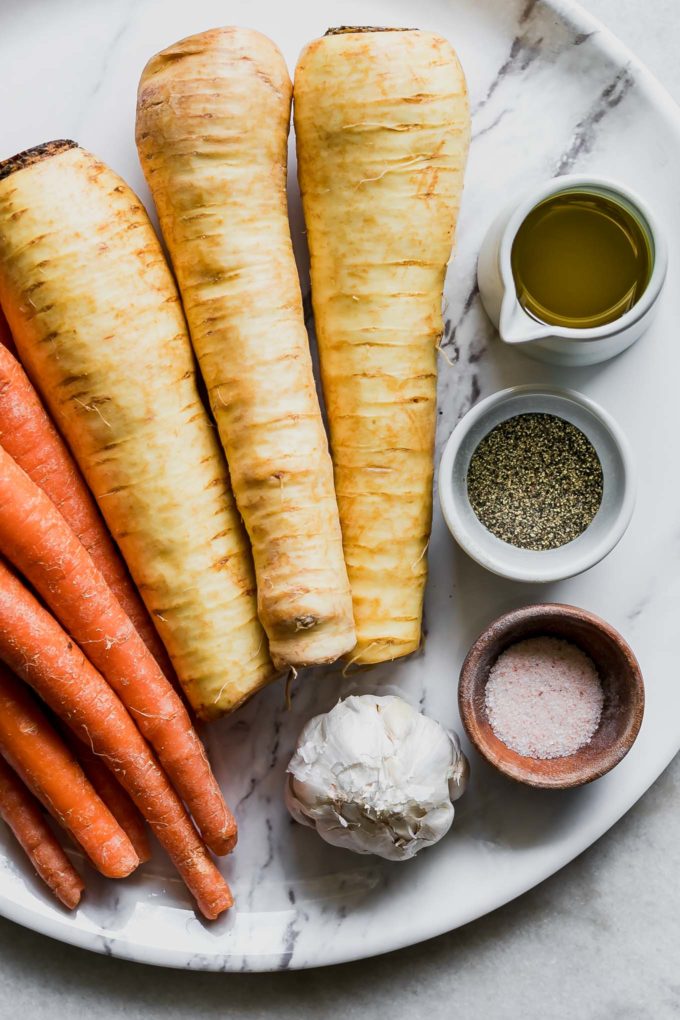 carrots, parsnips, and bowls of olive oil, salt, pepper, and garlic on a white table