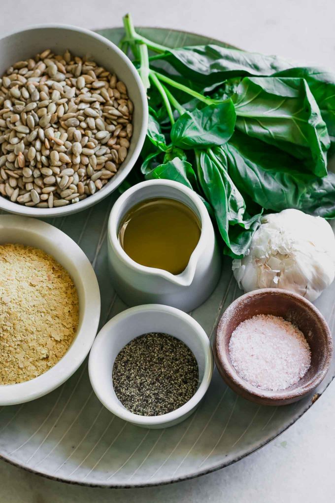 a bunch of basil and bowls of sunflower seeds, olive oil, cheese, garlic, salt, and pepper