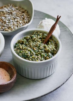 a bowl of sunflower seed pesto with a wooden spoon on a white table with sunflower seeds and salt