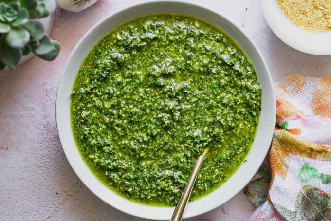 a bowl of cilantro pesto with a gold spoon on a pink tabletop