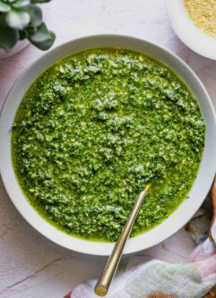 cilantro pesto in a bowl with a gold fork on a pink tablecloth