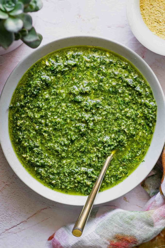 cilantro pesto in a bowl with a gold fork on a pink tablecloth
