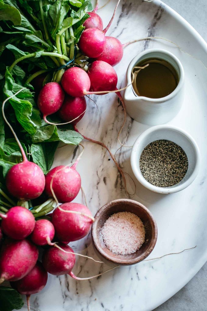 radishes and bowls of oil, salt, and pepper on a marble platter