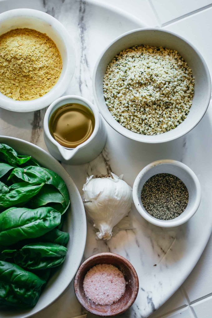 bowls of basil, cheese, oil, hemp seeds, salt, pepper, and garlic