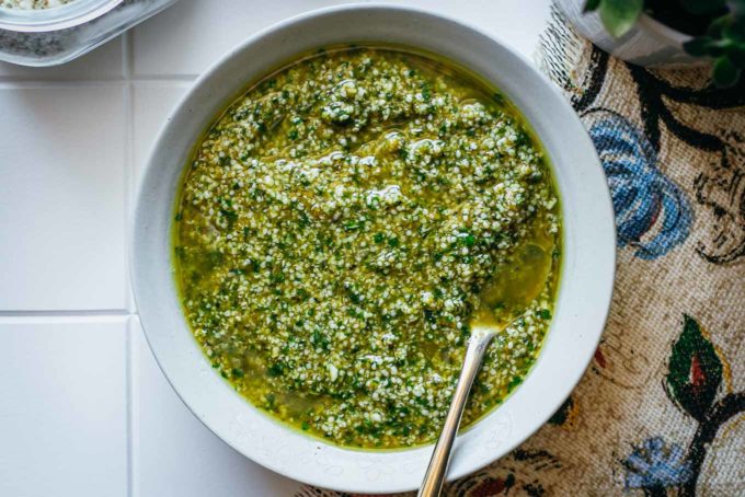 hemp seed pesto in a white bowl with a gold spoon on a tiled counter with a floral napkin