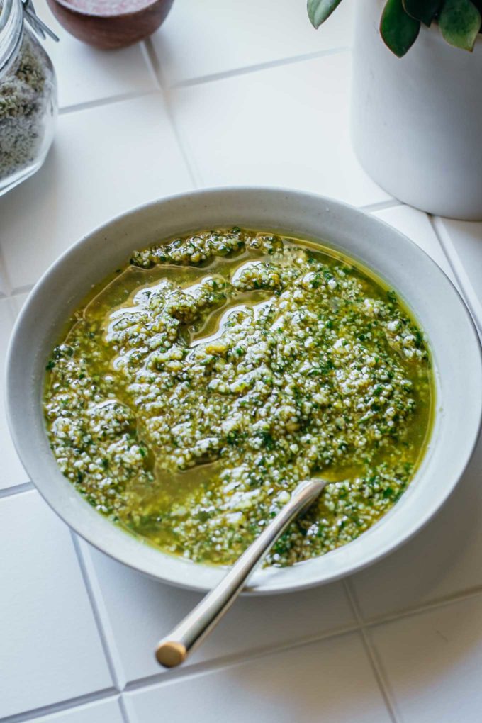 hemp seed pesto in a white bowl with a gold spoon on a tiled counter