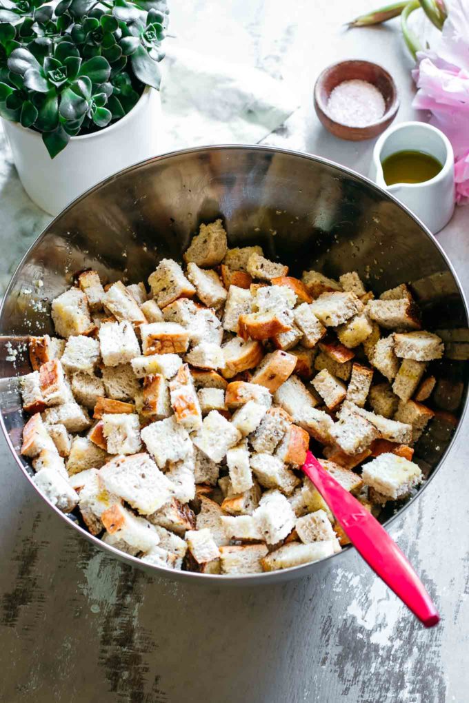 rye bread cubes in a mixing bowl with oil, salt, pepper, and a red spoon