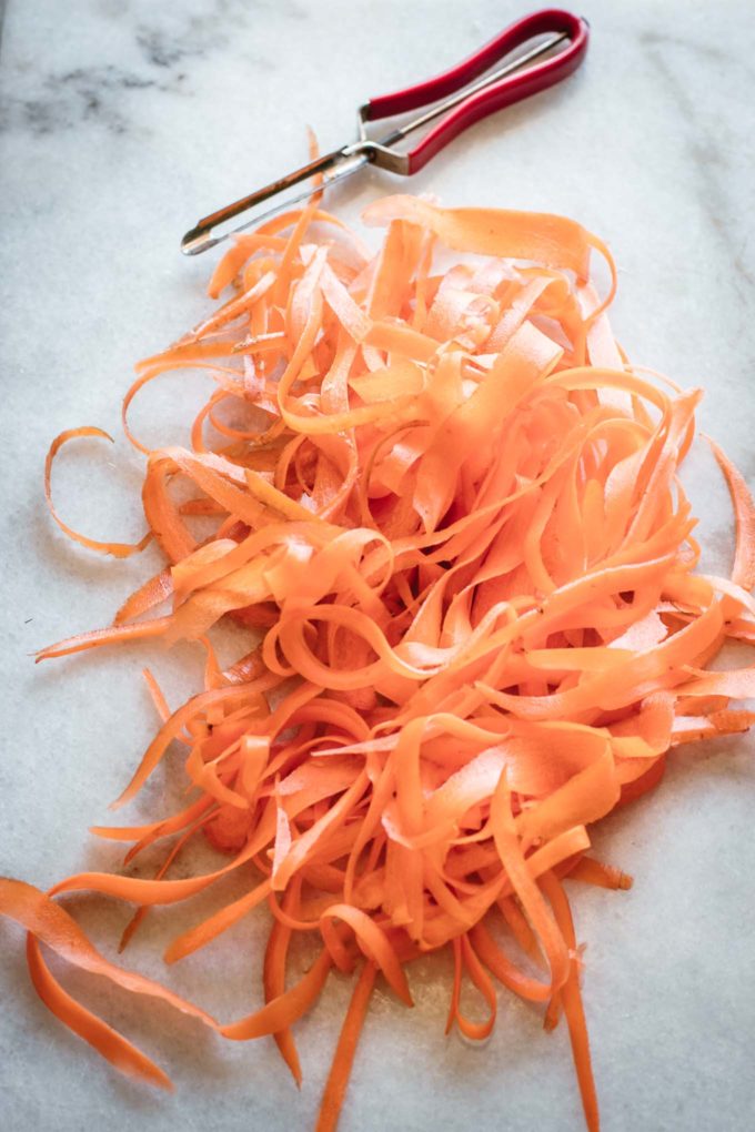 carrot ribbons and a vegetable peeler on a counter