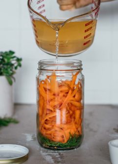 hot brine being poured into a jar of carrot ribbons, dill and other spices