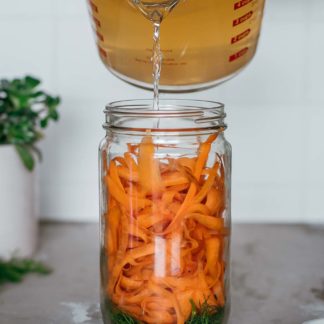 hot brine being poured into a jar of carrot ribbons, dill and other spices