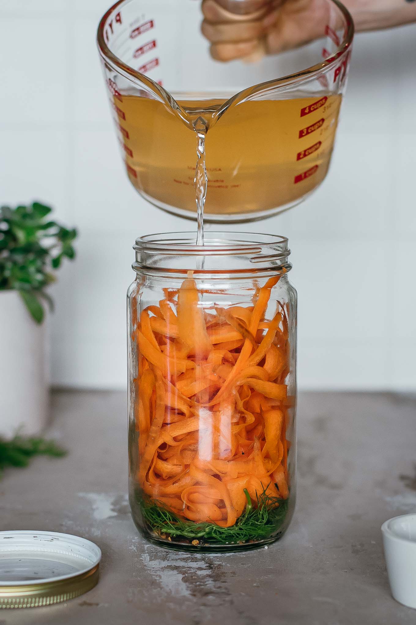 hot brine being poured into a jar of carrot ribbons, dill and other spices