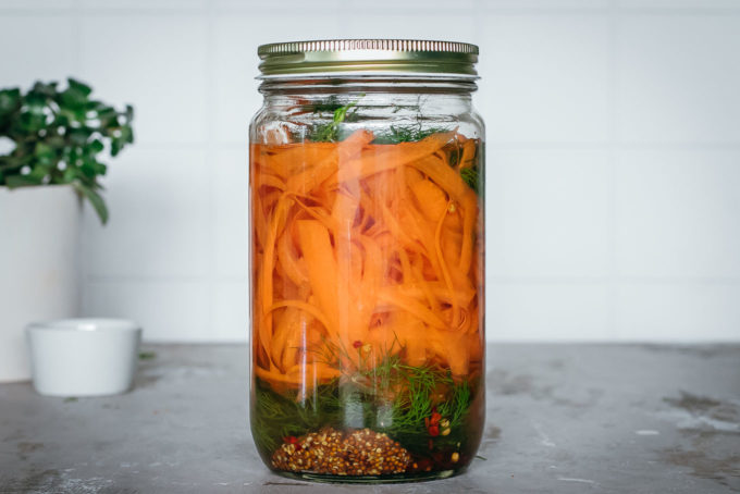 jar of pickled carrot peels and spices on a countertop