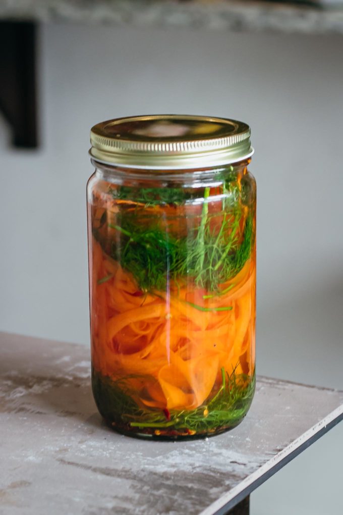 Sealed jar of carrot peels, dill and other spices on a table