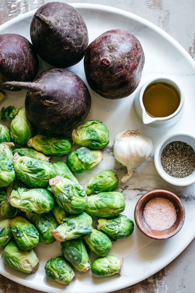 beets, brussels sprouts, garlic and bowls of oil, salt and pepper on a white platter