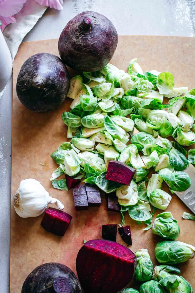 beets, garlic and chopped brussels sprouts on a cutting board with a knife