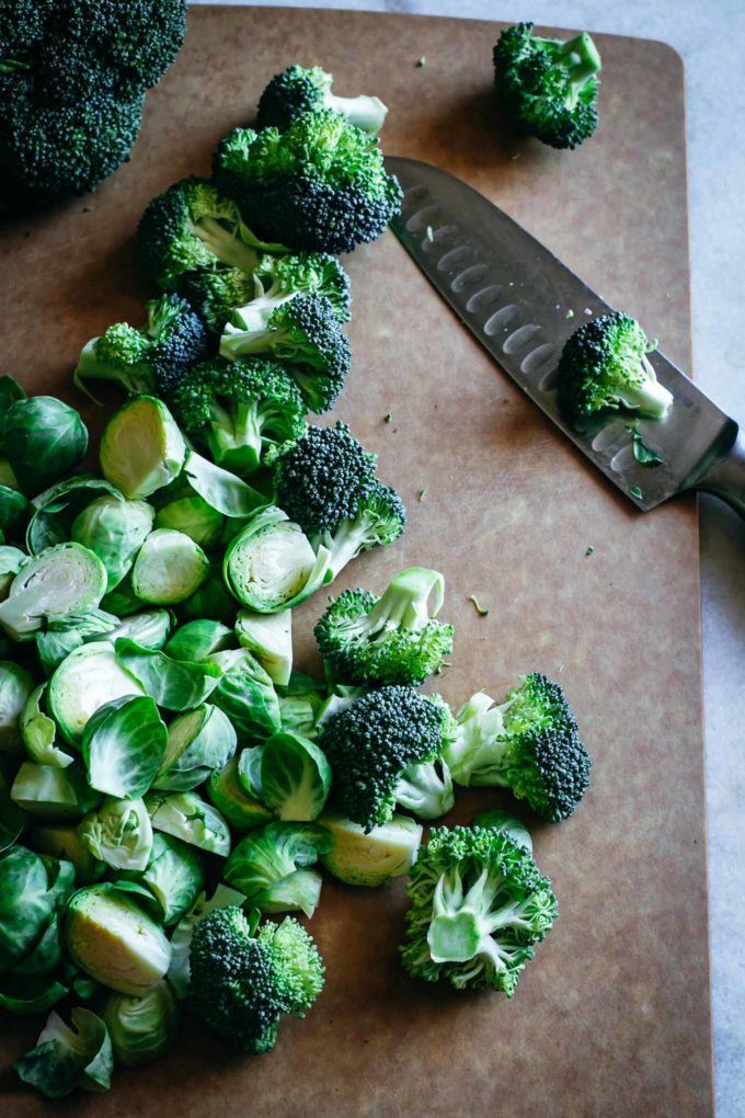 cut brussels sprouts and broccoli on a cutting board with a knife