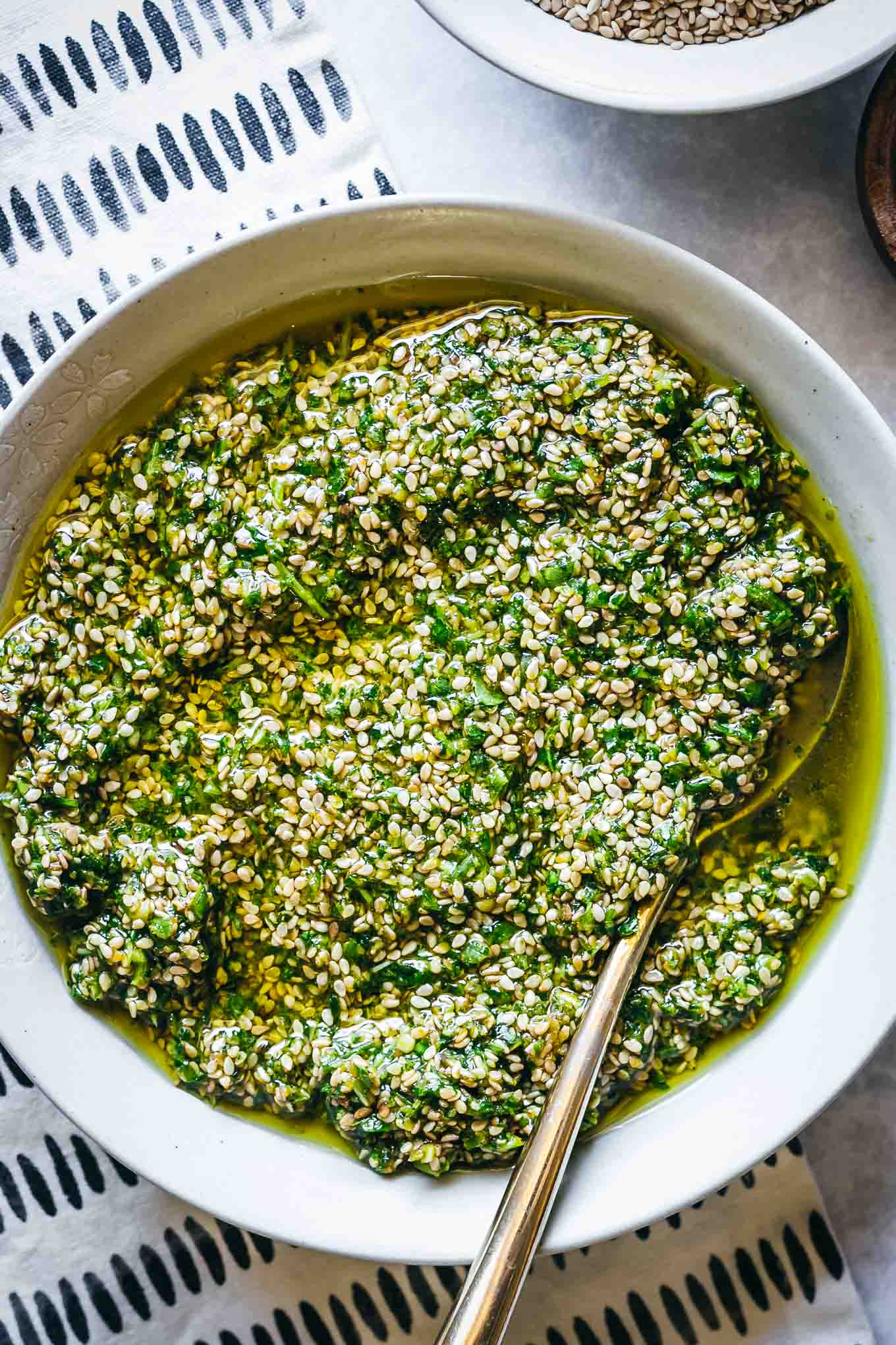 sesame seed pesto in a white bowl with a gold spoon