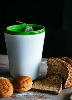 slices of bread and sliced buns next to a compost bin on a countertop