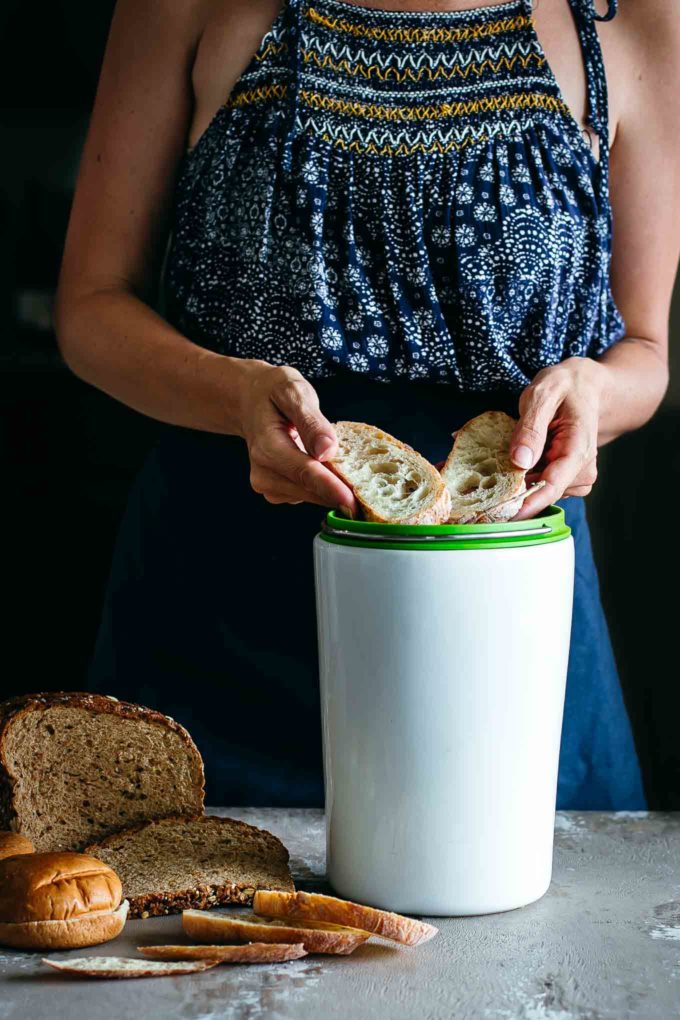 woman holding two slices of bread over a small compost bin