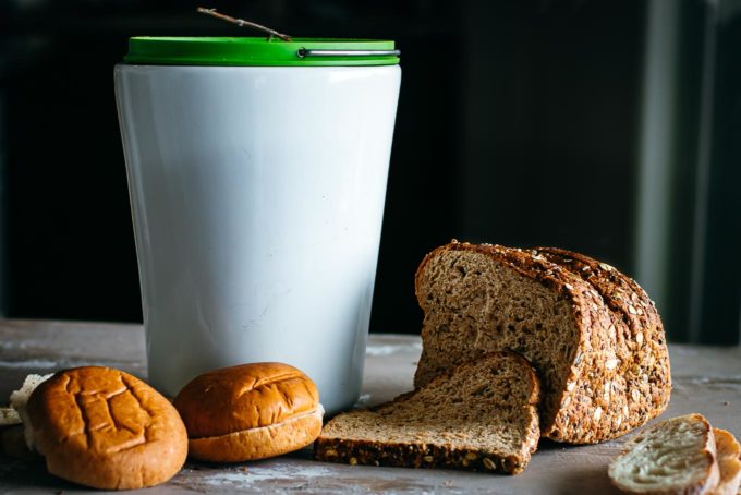 compost bin on a counter surrounded by various types of bread