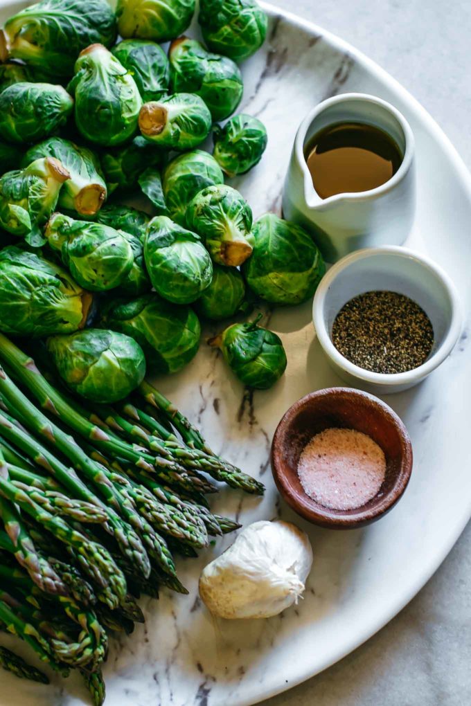 brussels sprouts, asparagus, garlic and bowls of olive oil, salt and pepper on a white table