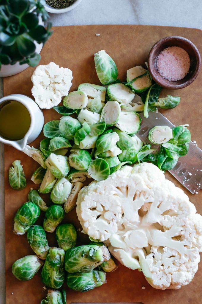 chopped cauliflower, brussels sprouts, and spices on a cutting board with a knife