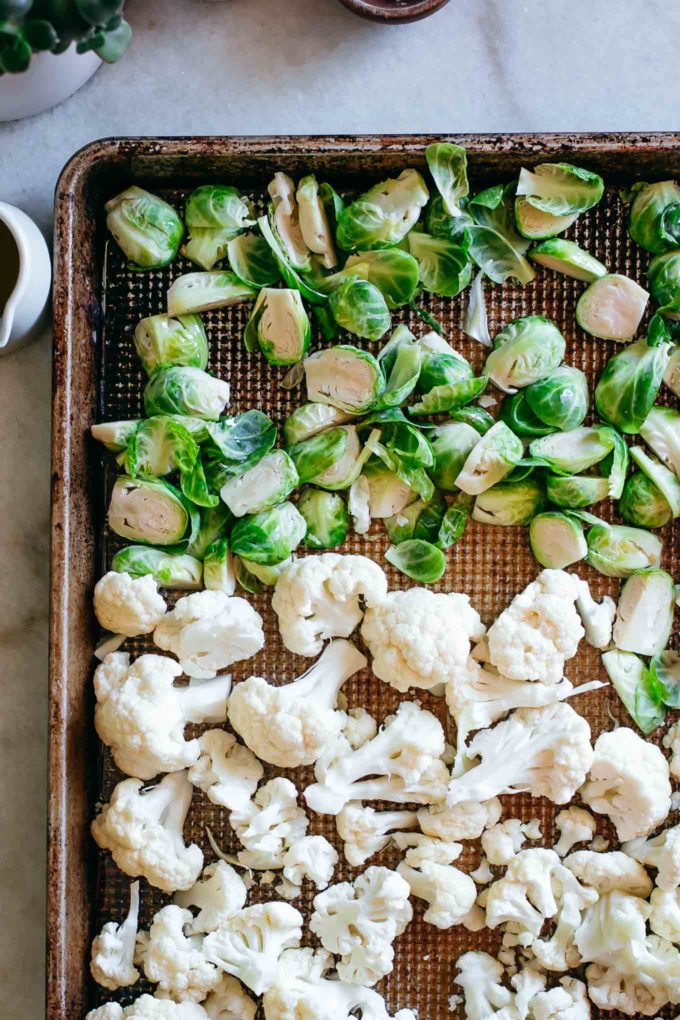 raw chopped brussels sprouts and cauliflower on a roasting pan