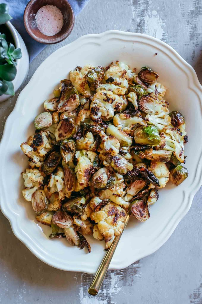 close up of roasted brussels sprouts and cauliflower on a platter with a gold spoon