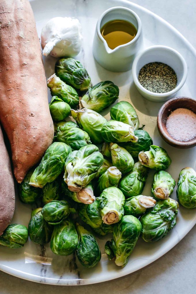 sweet potatoes, brussels sprouts, olive oil, garlic and spices on a plate