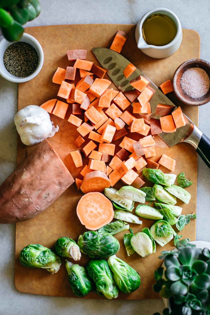 chopped sweet potatoes and brussels sprouts on a cutting board with a knife