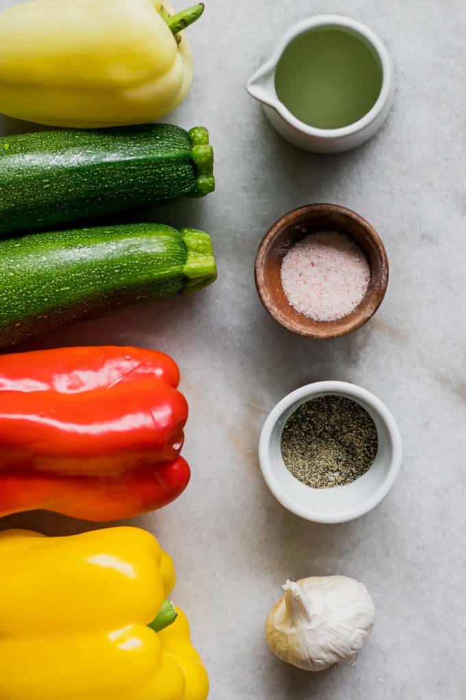 zucchini, bell peppers, and bowls of olive oil, salt, and pepper on a white table