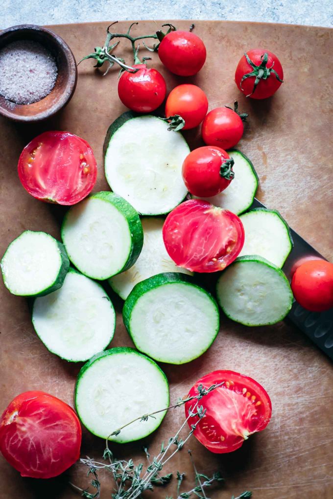 sliced zucchini and whole cherry tomatoes on a wood cutting board