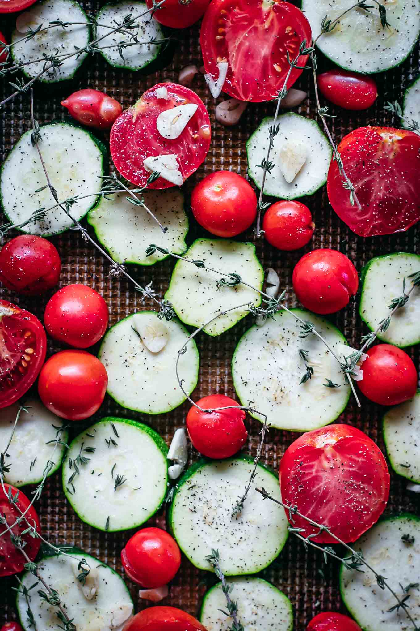 raw zucchini and tomatoes on a baking sheet before roasting