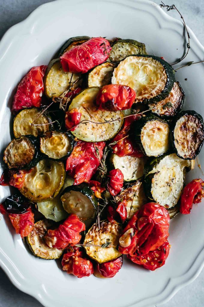 oven baked zucchini slices and cherry tomatoes on a white plate