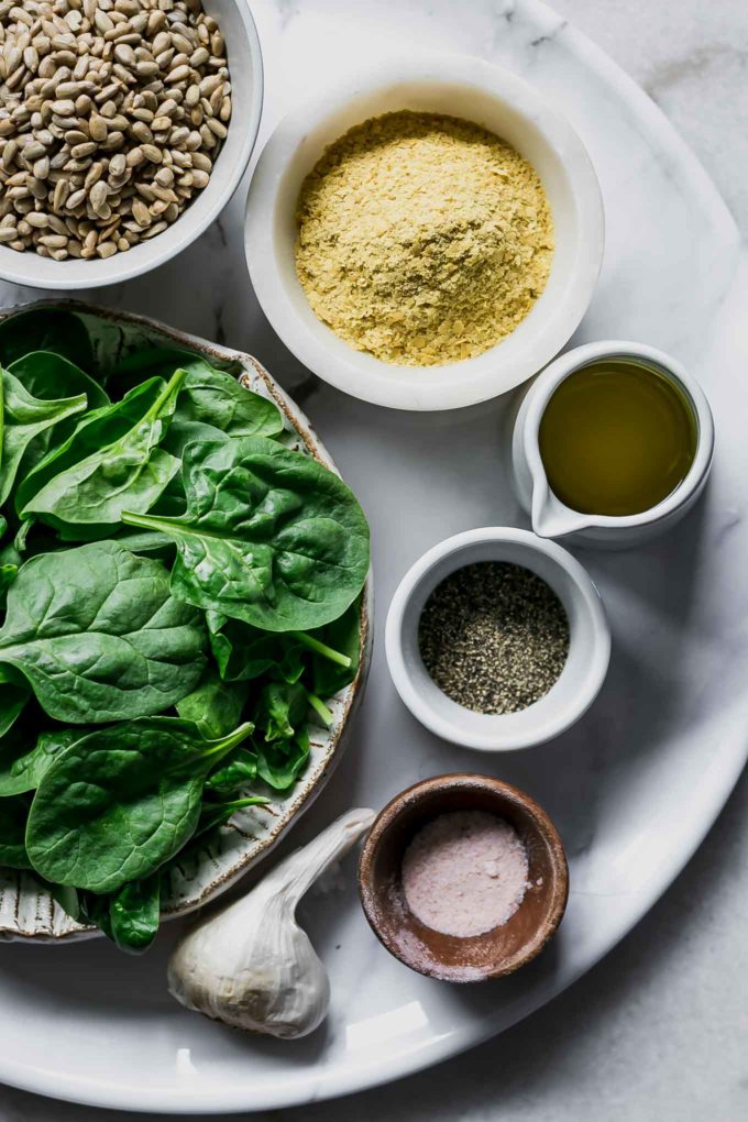 bowls of spinach leaves, seeds, nutritional yeast, olive oil, garlic, salt and pepper