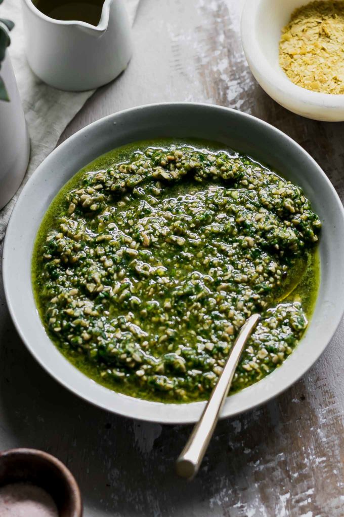 bowl of vegan spinach pesto on a countertop with a gold spoon