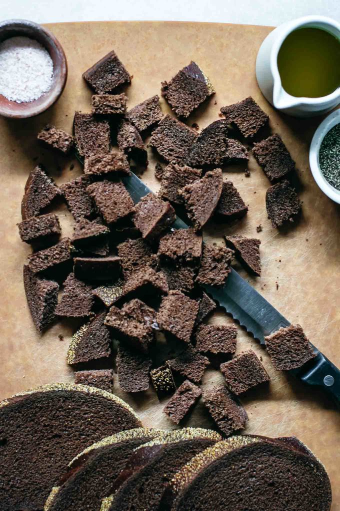 slices and cubes of pumpernickel bread on a cutting board with a serrated knife