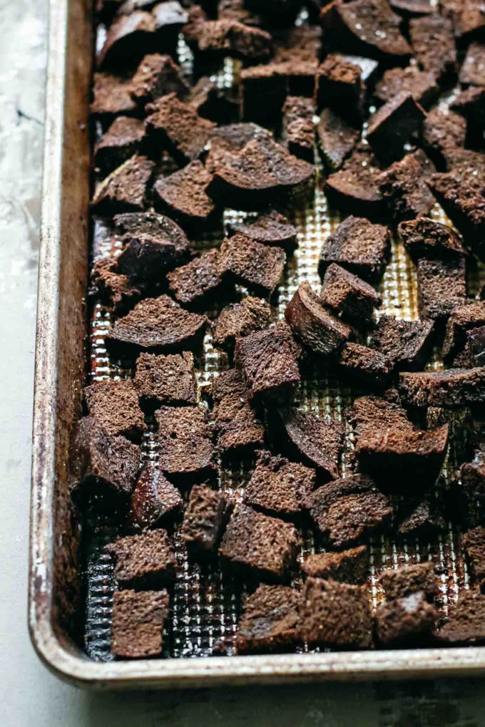 uncooked seasoned pumpernickel croutons on a baking sheet