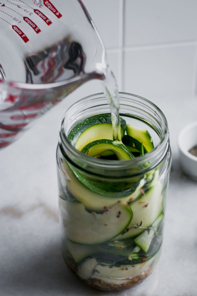 pickling brine pouring into a jar filled with sliced zucchini